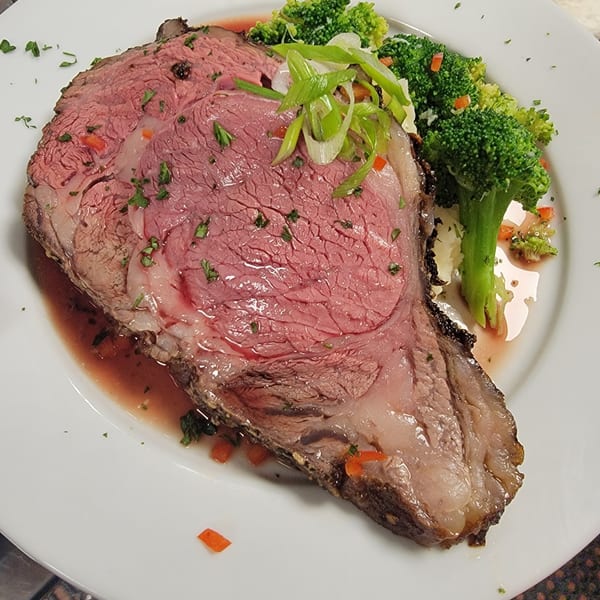 A thick slice of rare prime rib with gravy, garnished with broccoli and scallions.
