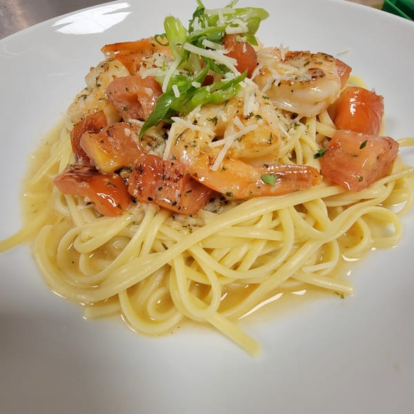 Linguine pasta with shrimp, diced tomatoes, grated cheese, and green onions on a white plate.